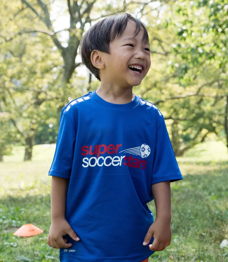 A smiling Soccer Stars player stands on a sunny field