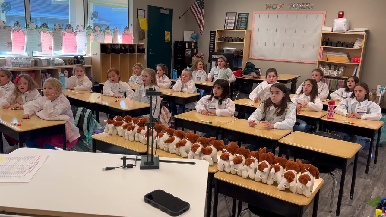 Little Veterinarian School students sit in lab coats beside rows of stuffed dogs