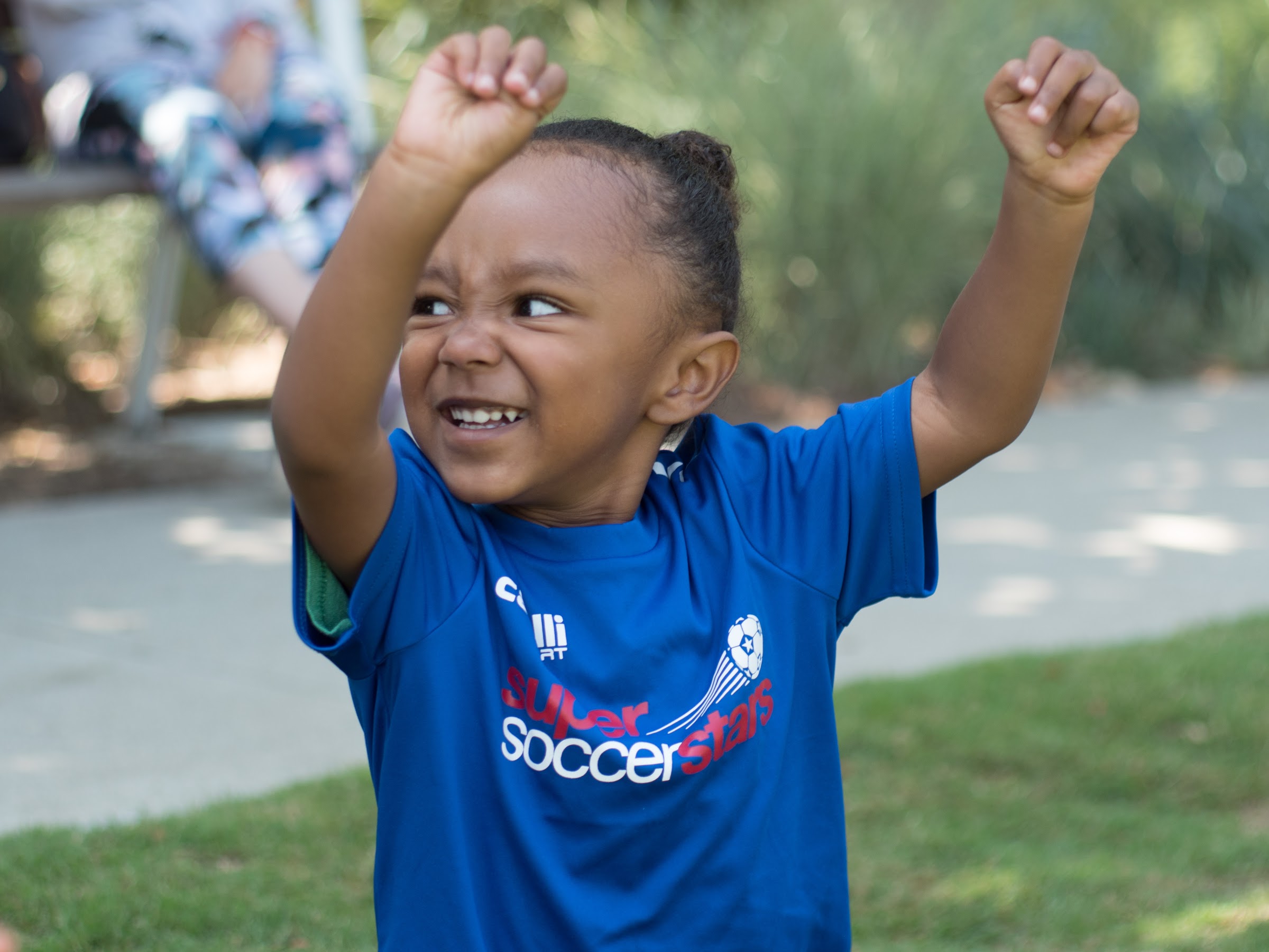 A young player raises both arms and smiles on a sunny field
