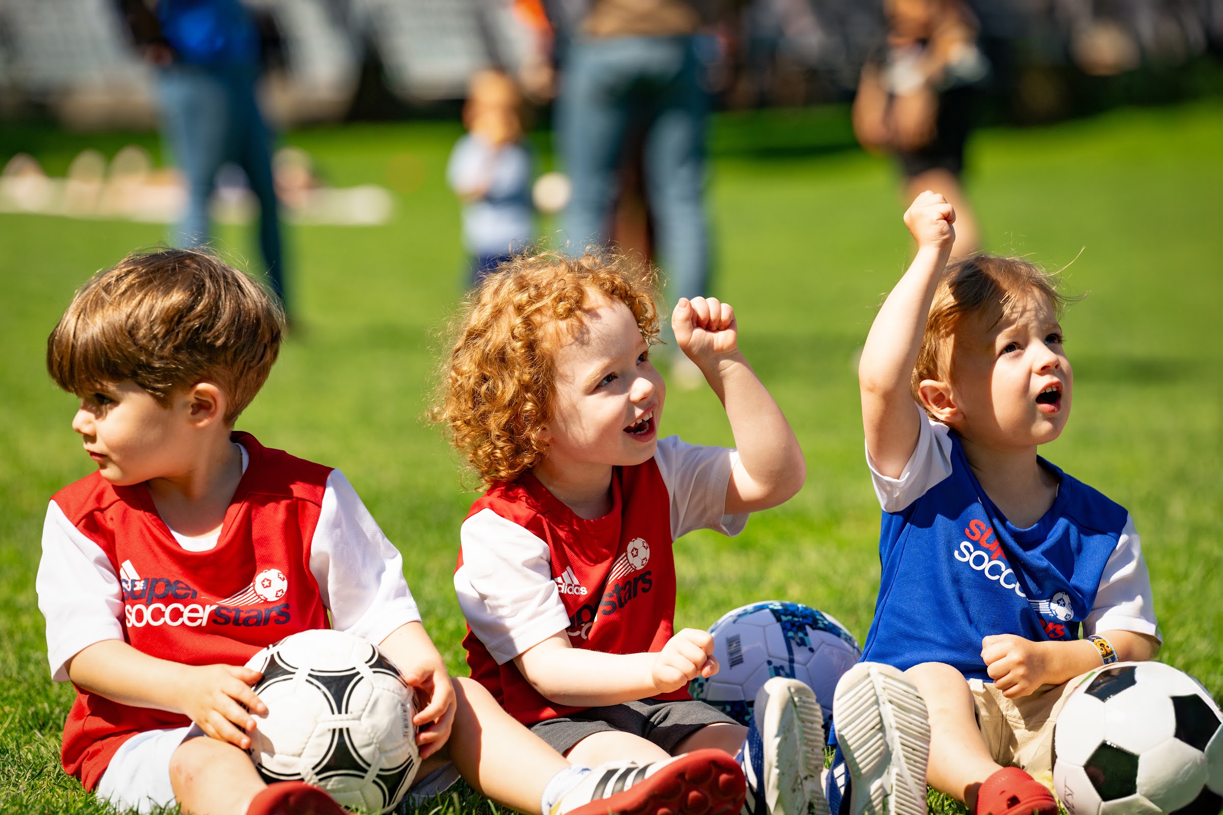Three preschool soccer players sit with their soccer balls